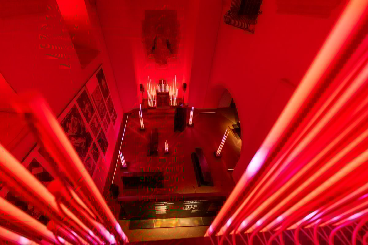 Pohled z ochozu na audiovizuální instalaci v Kapli křížů, nasvícenou červenými světelnými prvky.