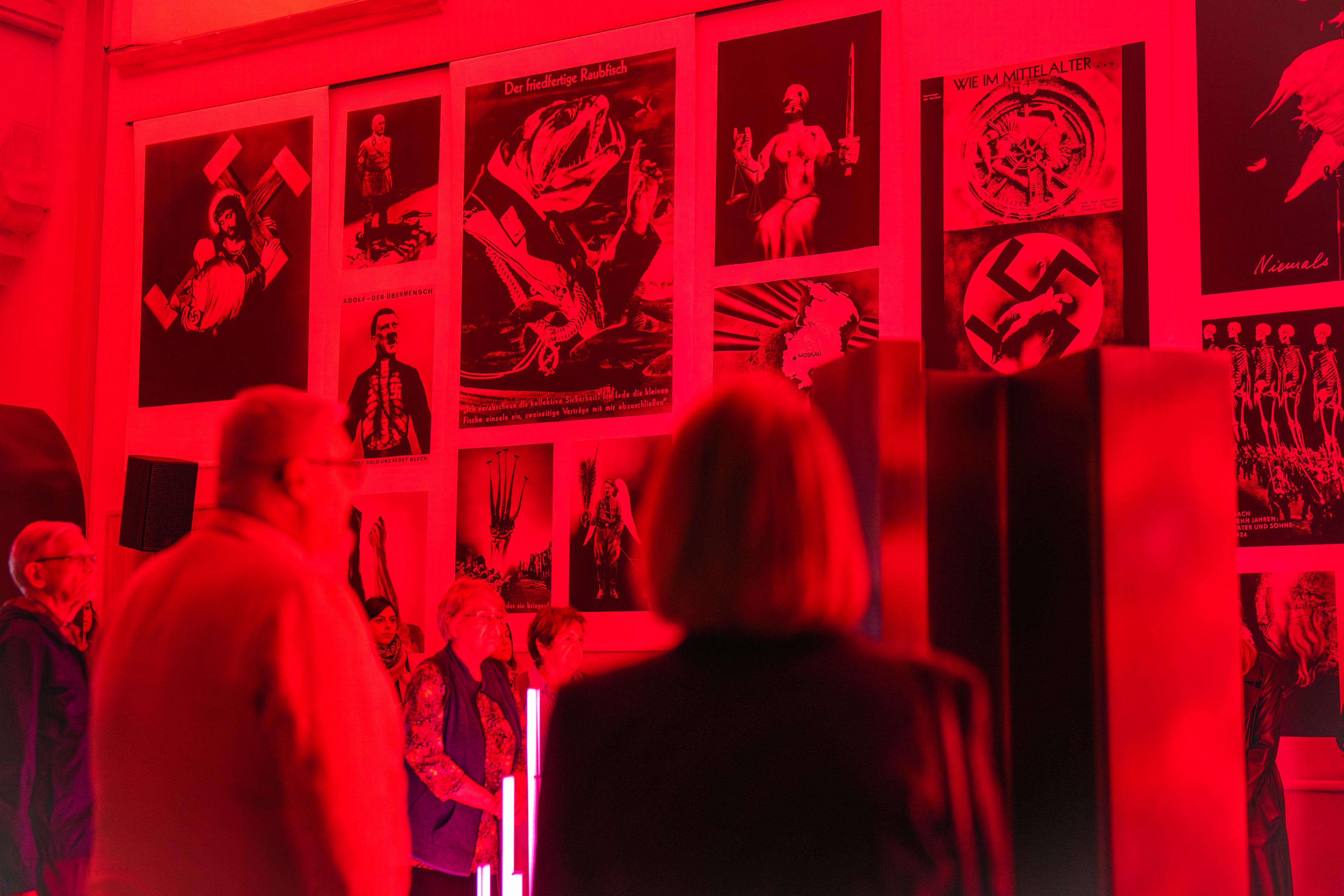 Návštěvníci v červeném světle instalace, tváří v tvář historii.