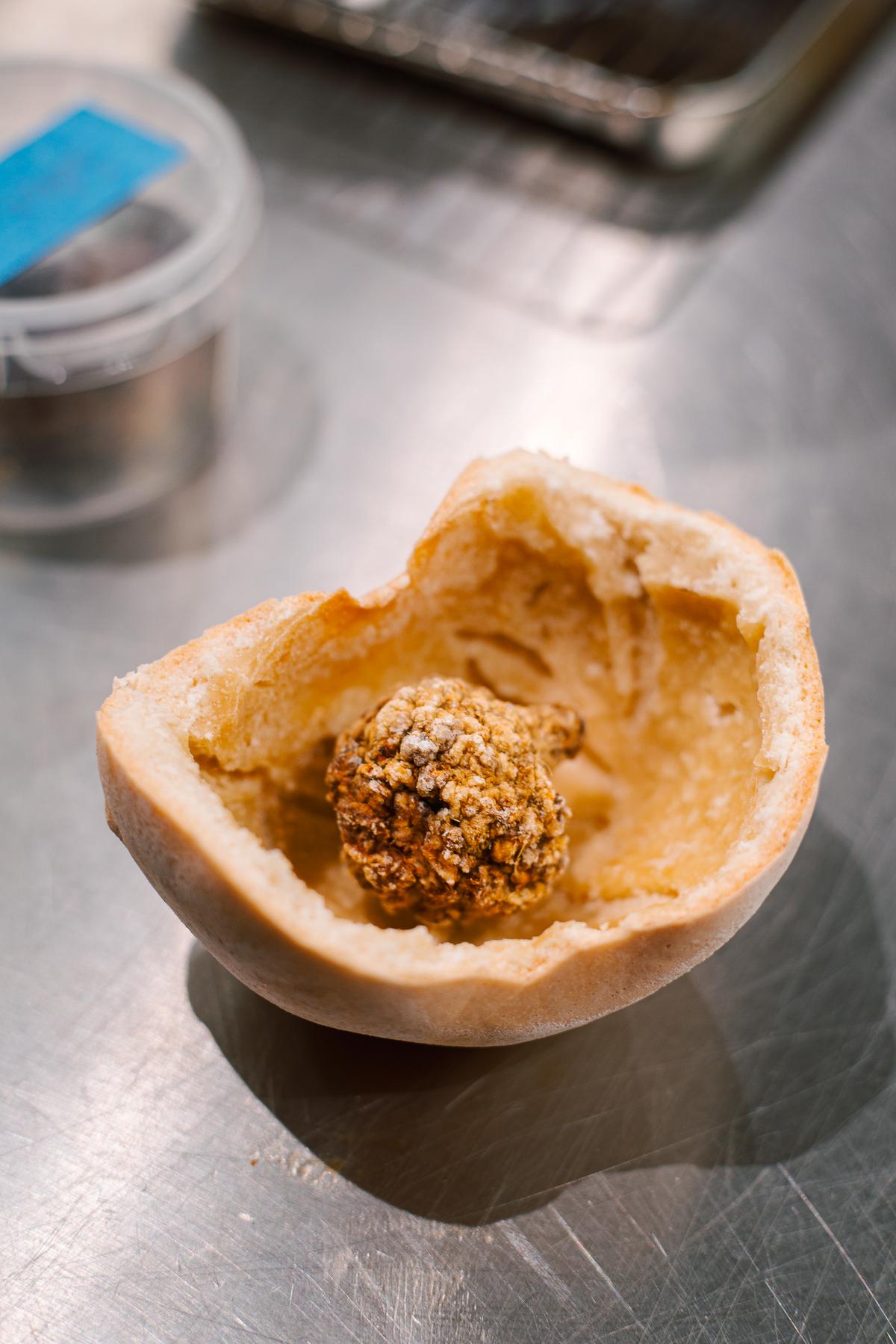 Malá kulička smaženého jídla vložený do rozkrojené housky na nerezovém povrchu.