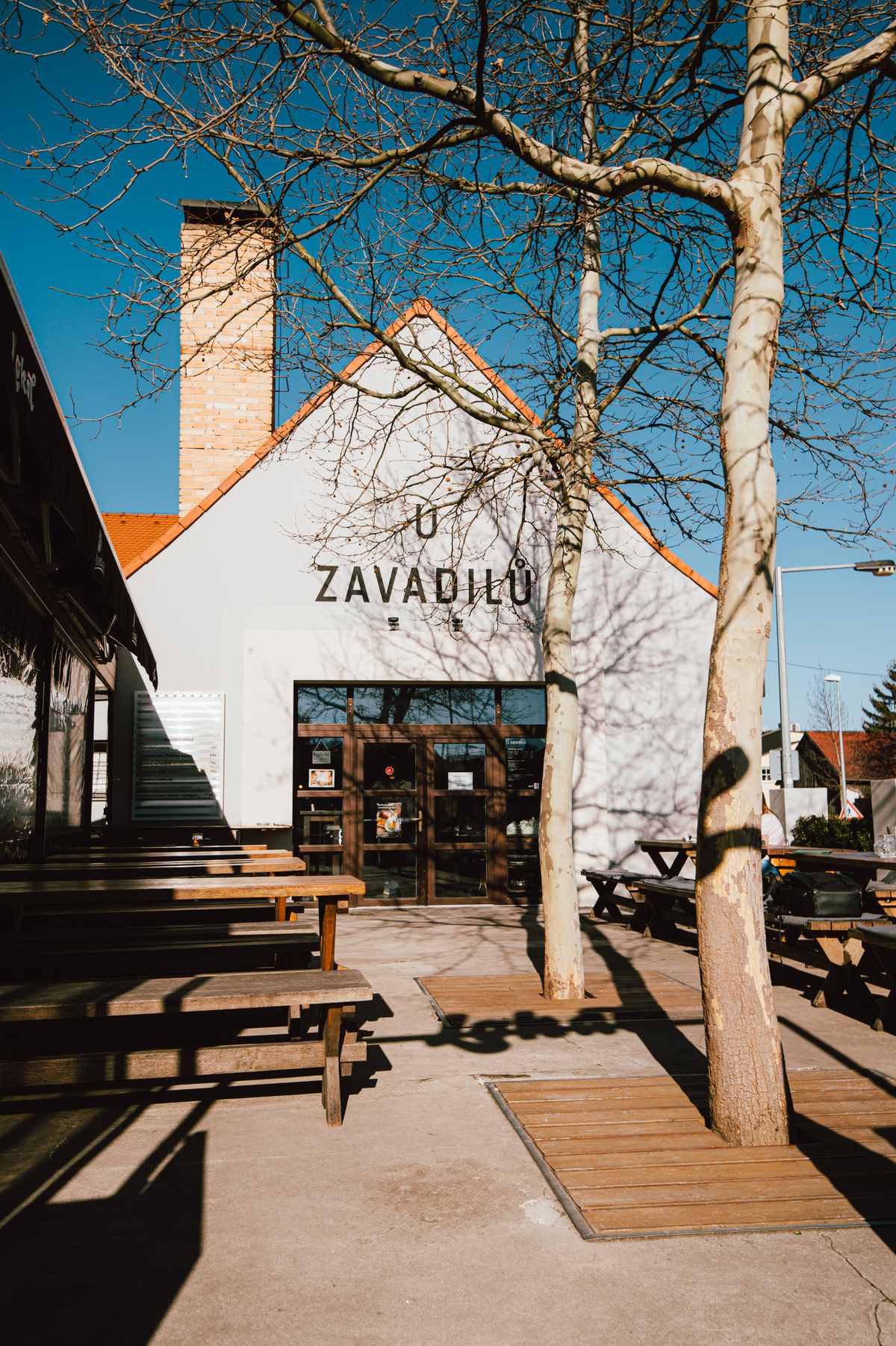 Zahrádka restaurace U Zavadilů s dřevěnými stoly a hosty.