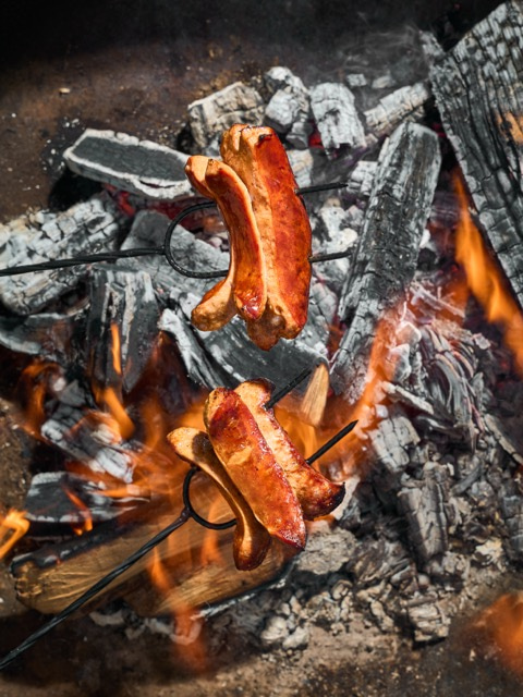 Špekáčky opékané nad ohněm na kovových vidlicích.