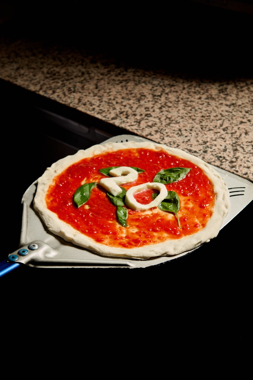 Pizza s rajčatovým základem, bazalkou a mozzarellou ve tvaru čísla 20, připravená v peci.