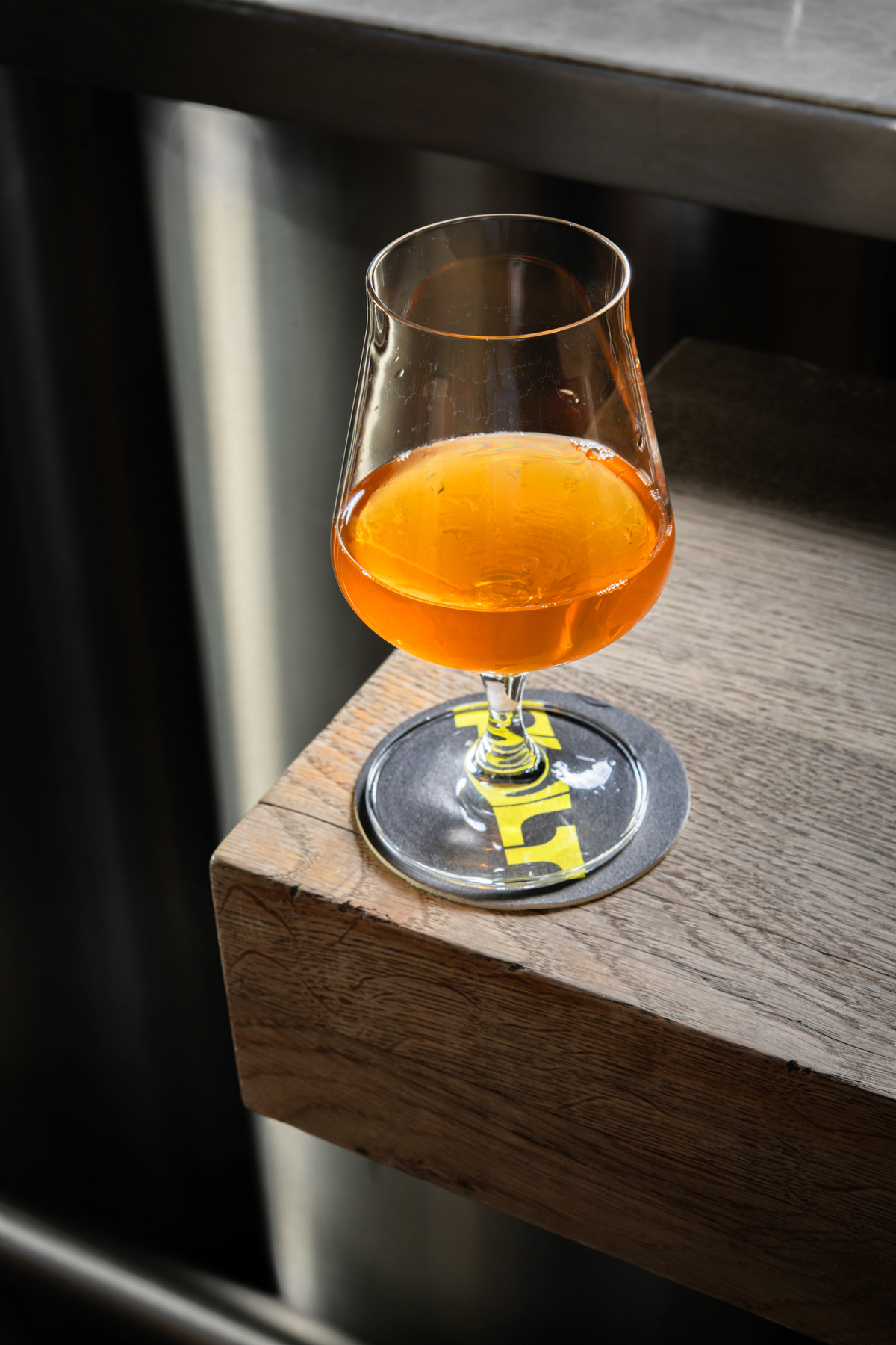 Sklenice světlého craftového piva na dřevěném barovém pultu.