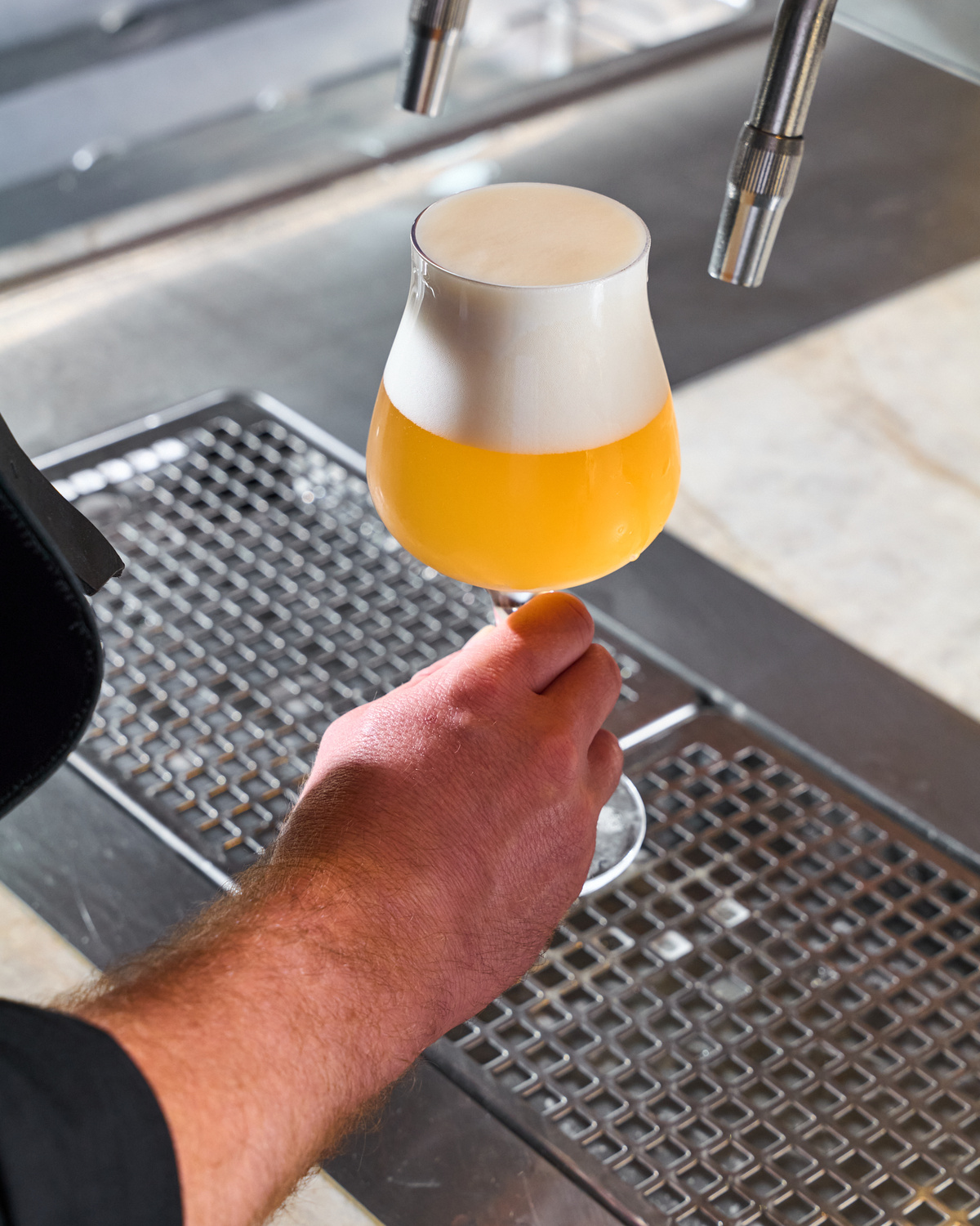 Výčepní drží sklenici craftového piva s hustou pěnou pod výčepním kohoutem.