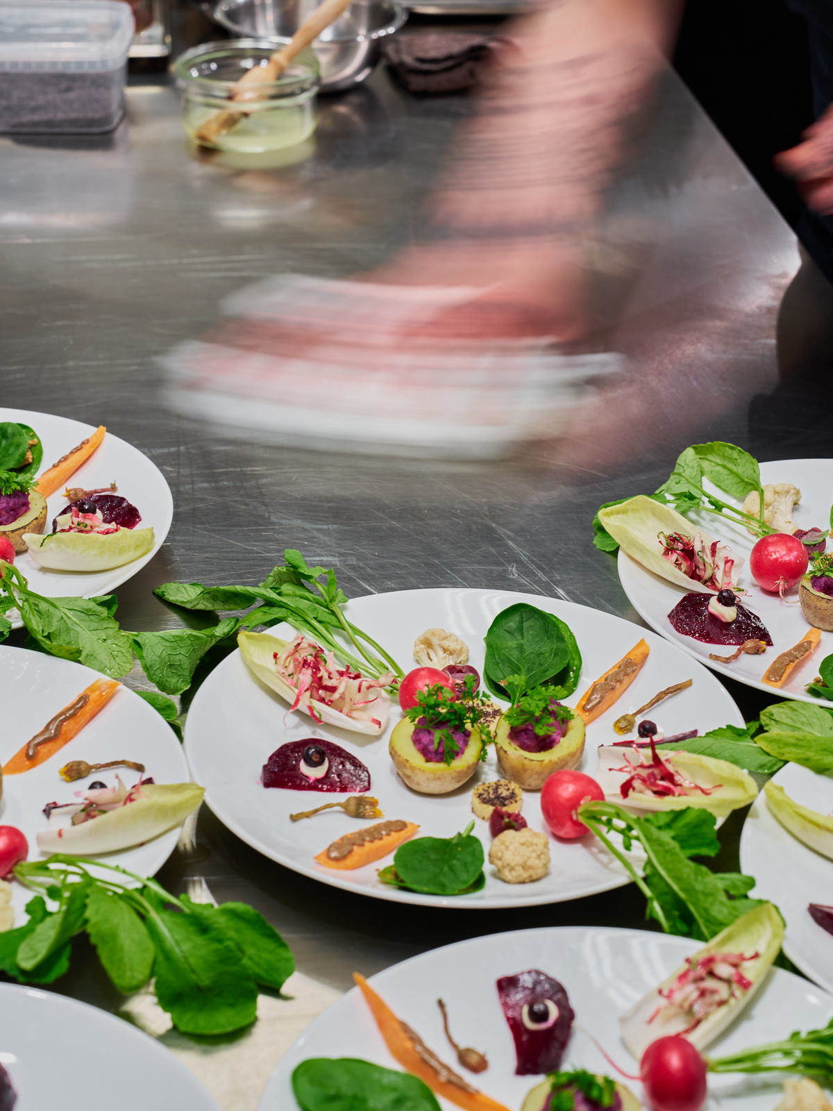 Šéfkuchař dokončuje plating několika talířů s moderní zeleninovou úpravou v kuchyni.