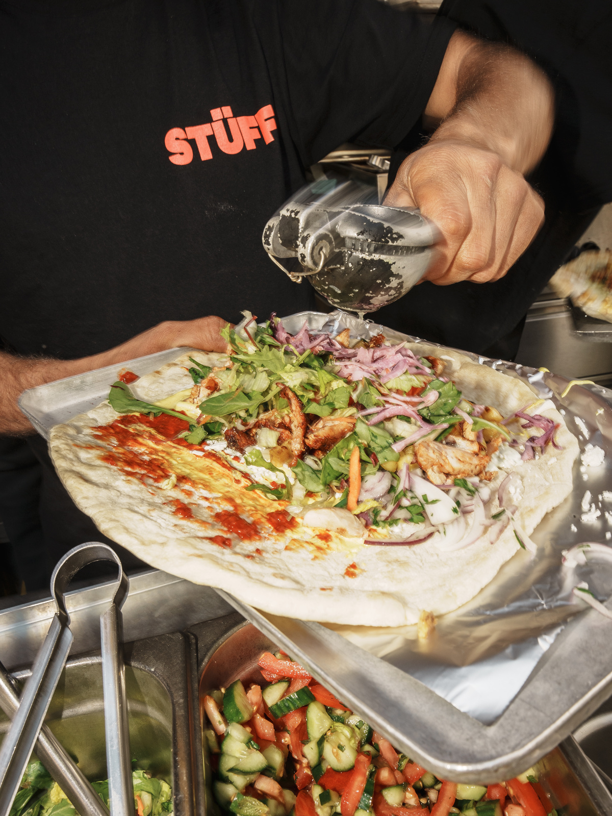 Kuchař připravuje velký dürüm kebab plněný masem, zeleninou a omáčkou na grilu streetfood stánku.