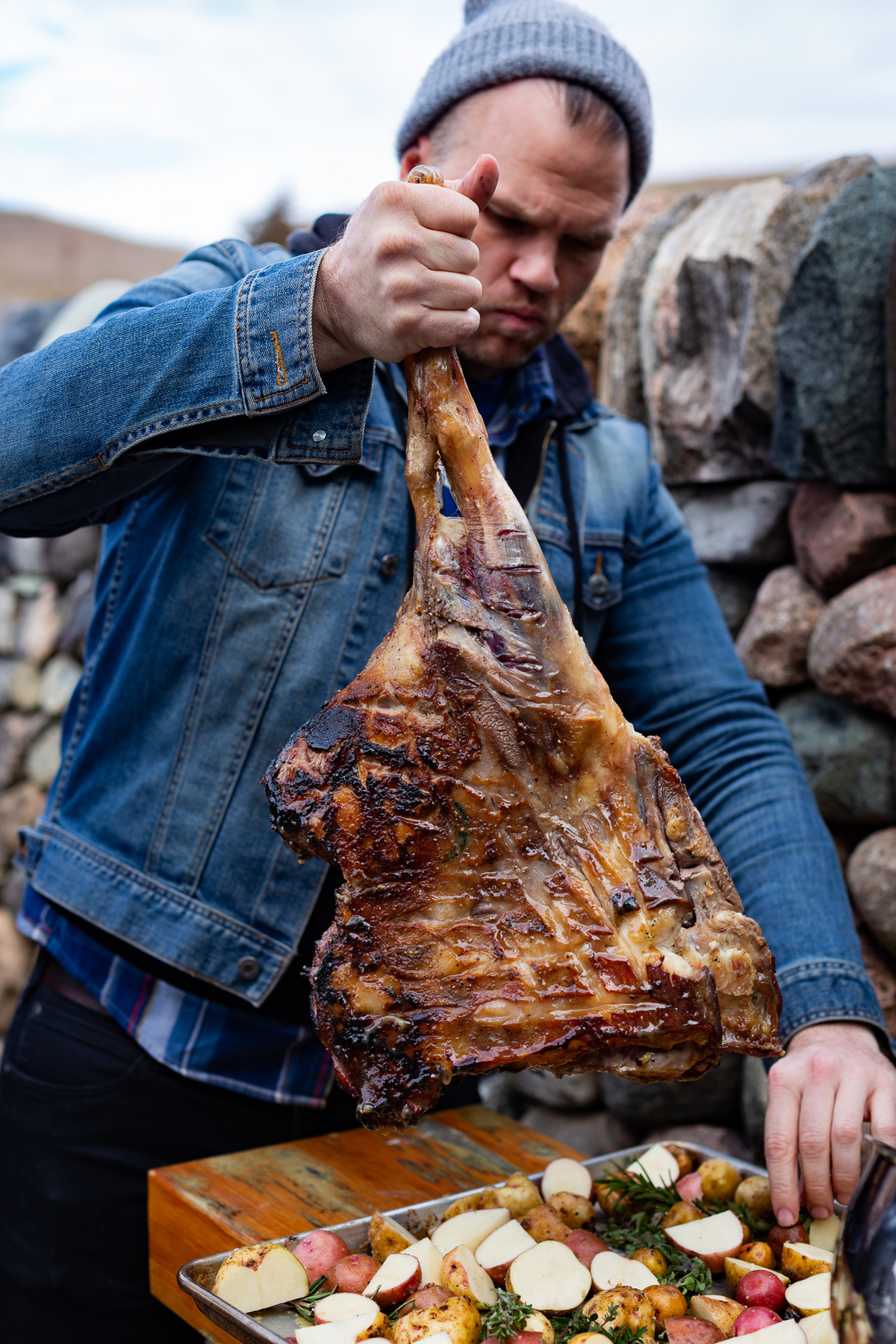 Kuchař drží velký grilovaný hovězí tomahawk steak nad plechem s pečenou zeleninou a ovocem.