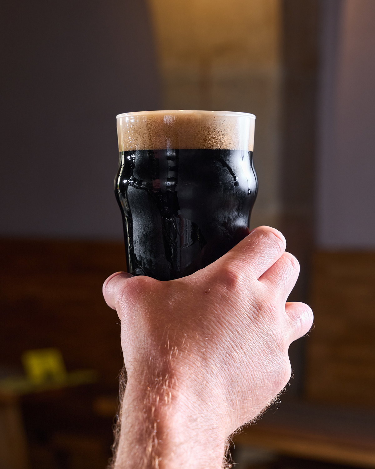 Sklenice Guinness s krémovou pěnou držená v ruce.