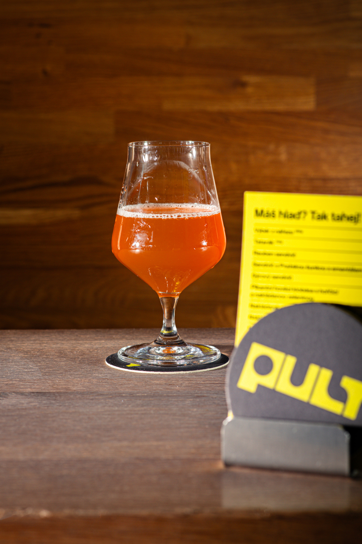 Sklenice červeného craftového piva na barovém pultu s rozmazaným menu v pozadí.