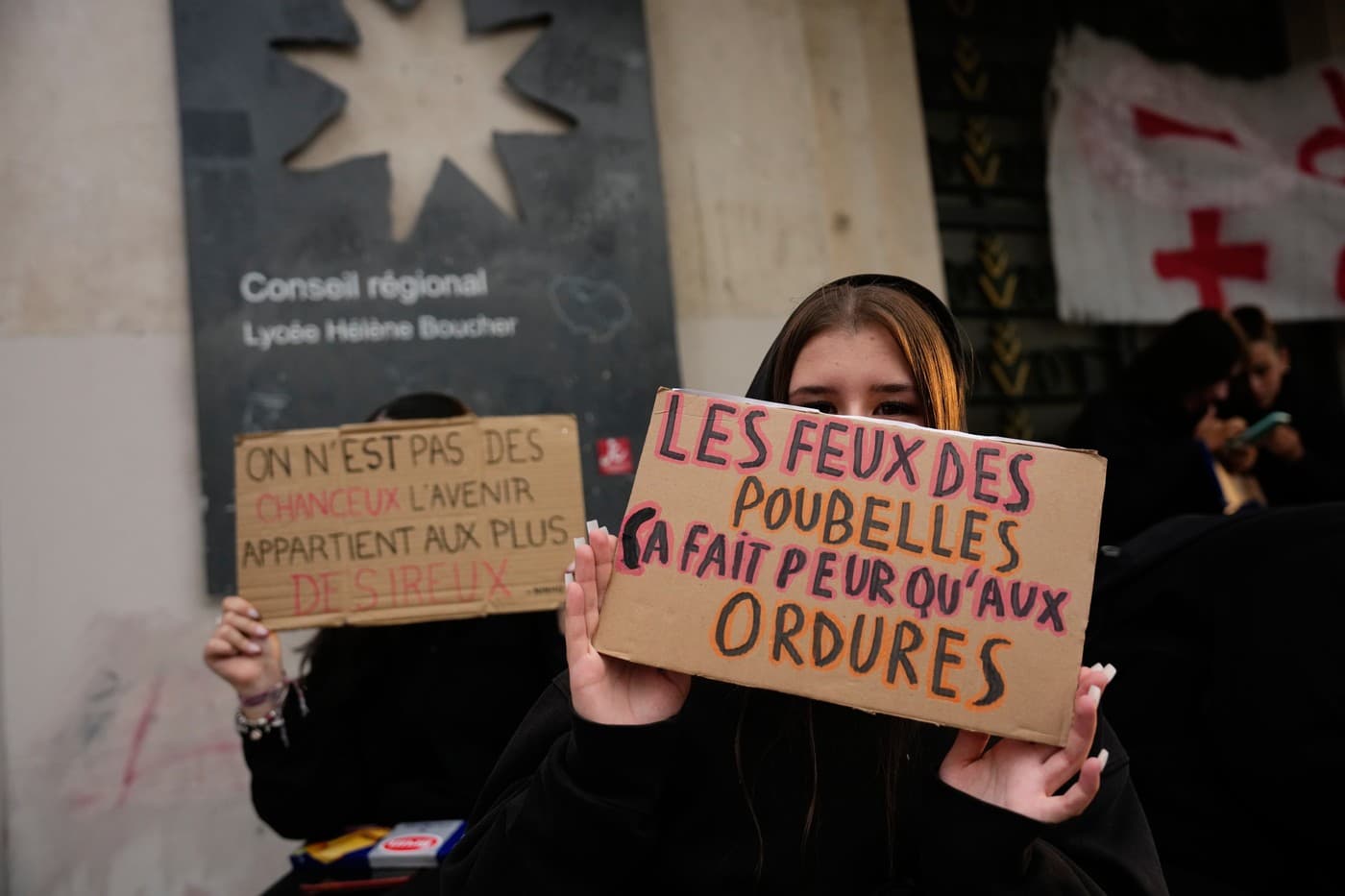  Studentka drží ceduli s nápisem „Požáry odpadků děsí jen odpadky“, zatímco stojí před zablokovanou střední školou v Paříži a protestuje proti nedostatečnému financování škol