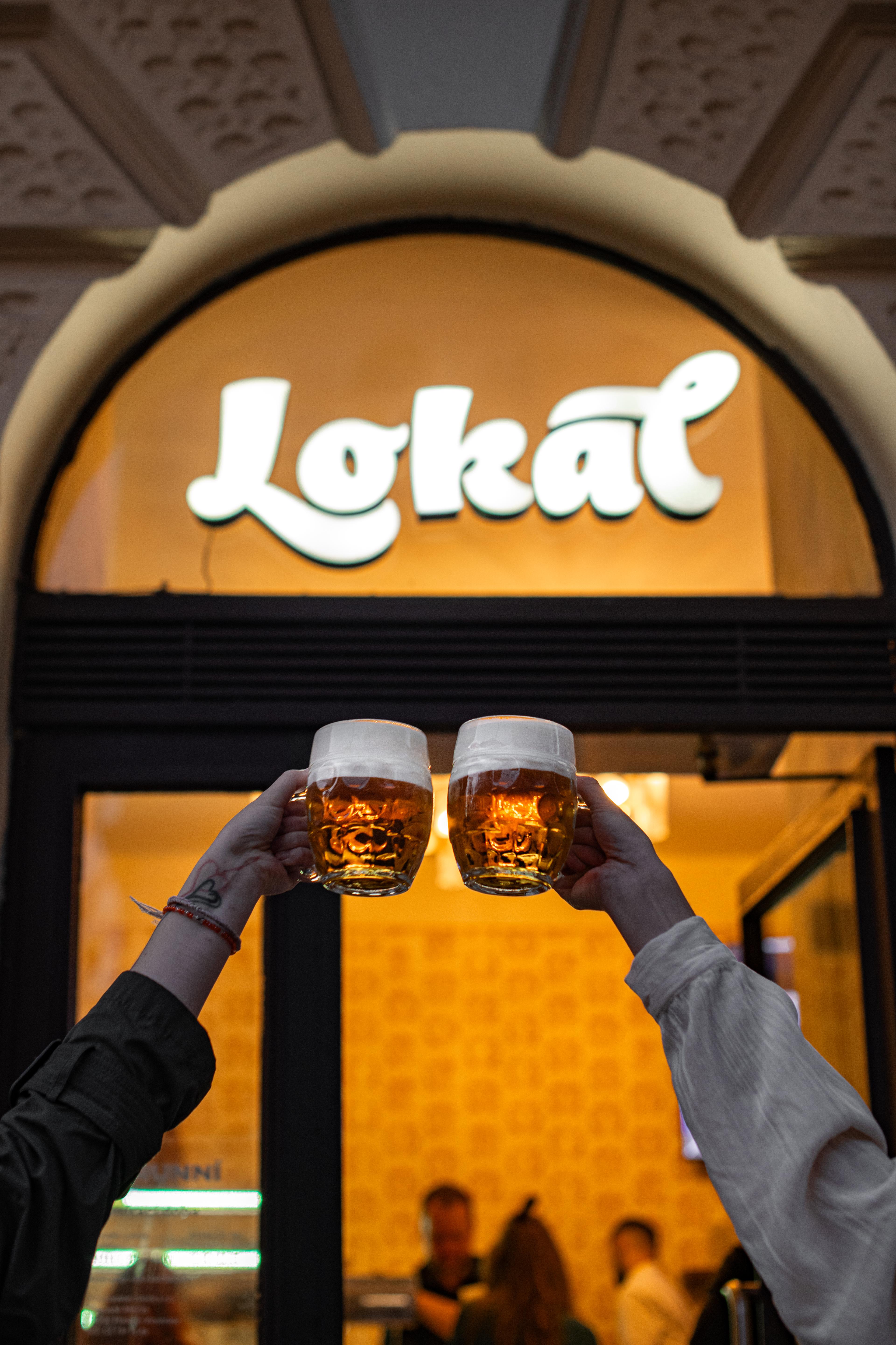 Dvě ruce si přiťukávají půllitry piva před Lokálem.