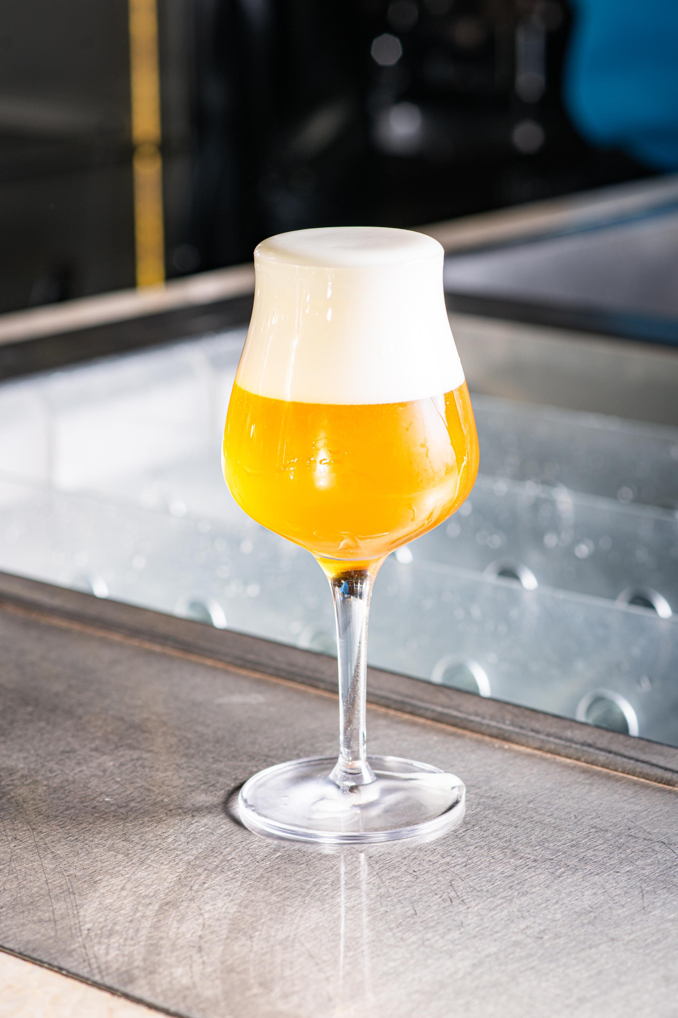 Sklenice světlého craftového piva s hustou pěnou na barovém pultu.