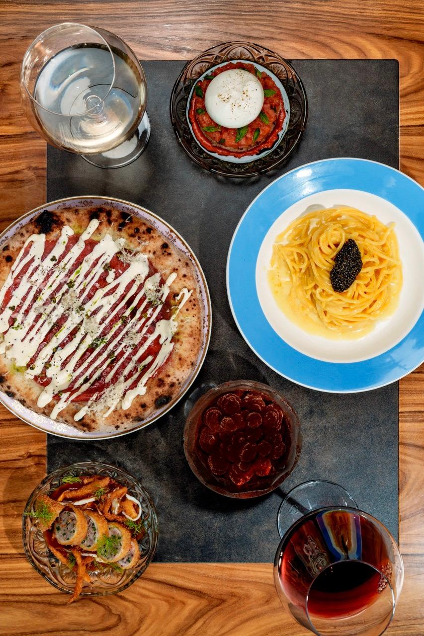 Pohled shora na stůl s pizzou, těstovinami s kaviárem, předkrmy a sklenkami vína.