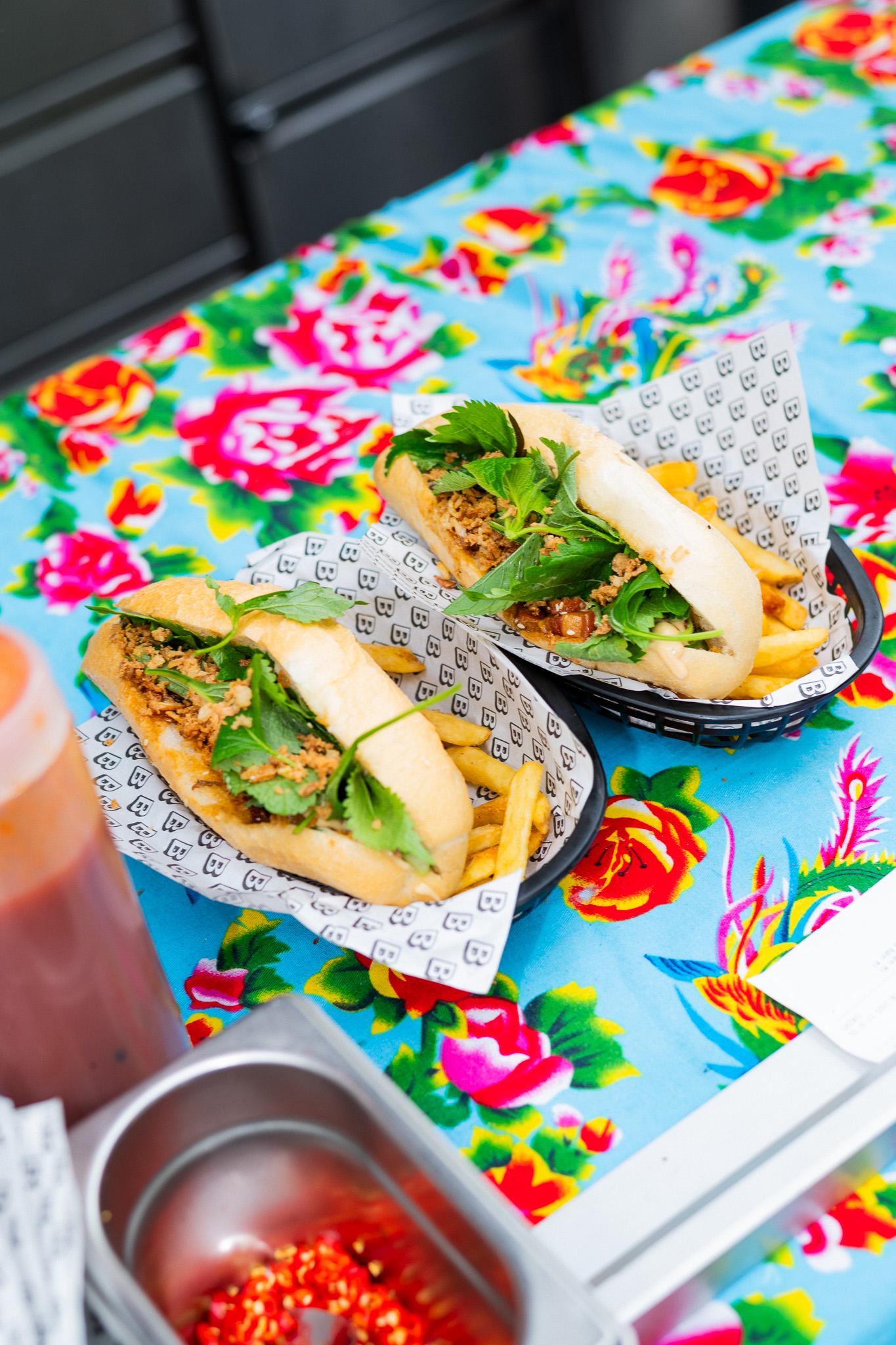 Dvě vietnamské bagety bánh mì s hranolkami na barevném květovaném ubrusu.