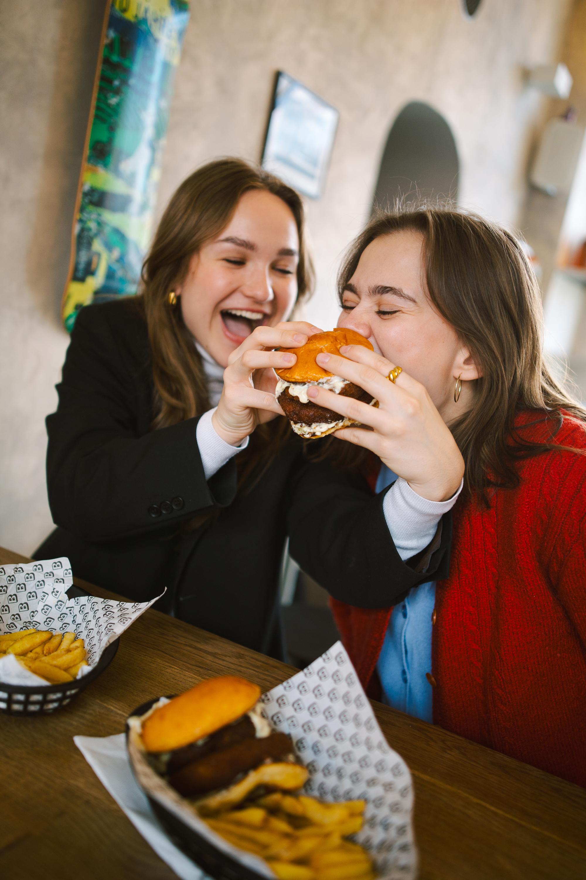 Dvě ženy si společně užívají velký burger a hranolky při oslavě Tučného čtvrtka v podniku Ambiente