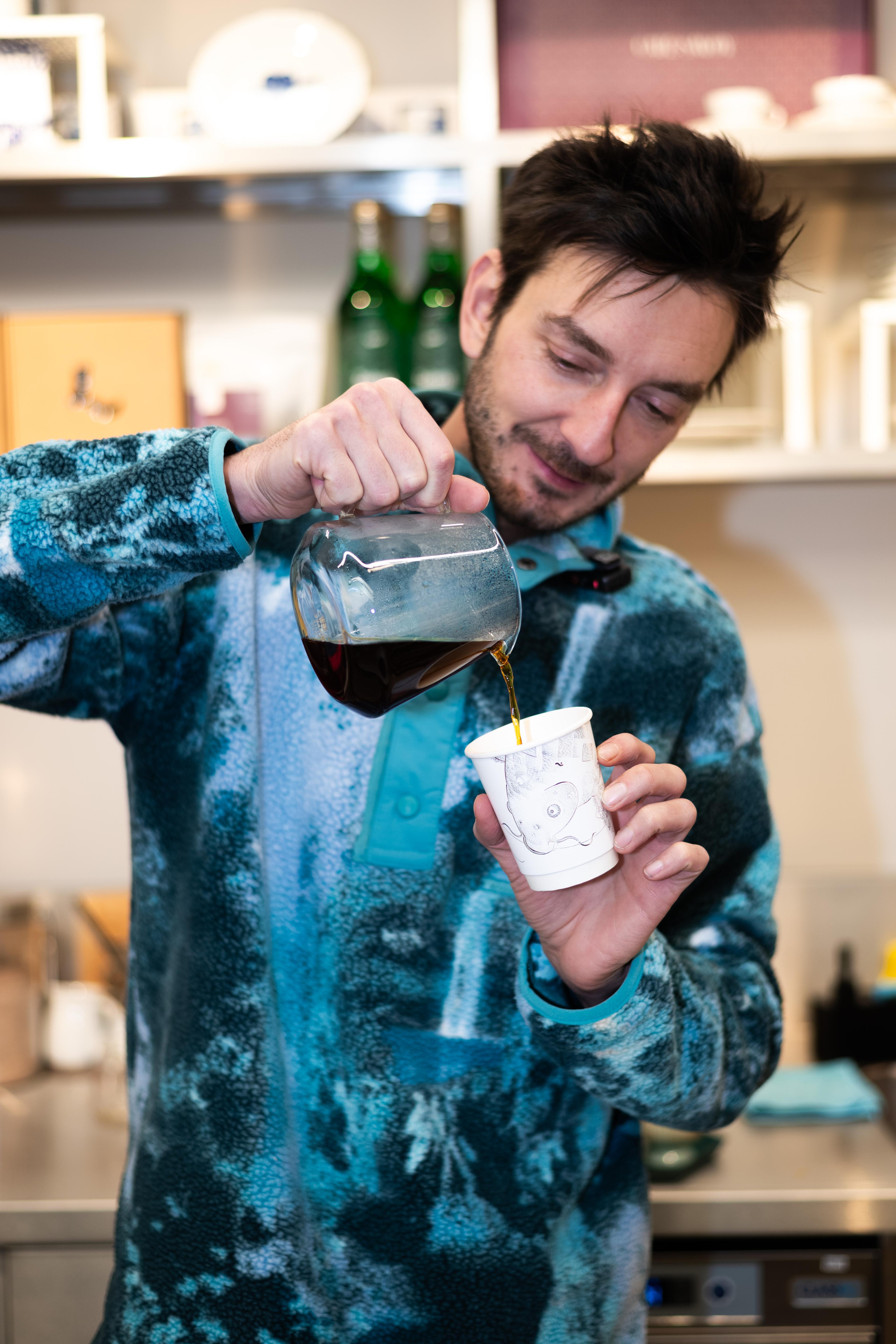 Barista nalévá filtrovanou kávu z konvičky do papírového kelímku.