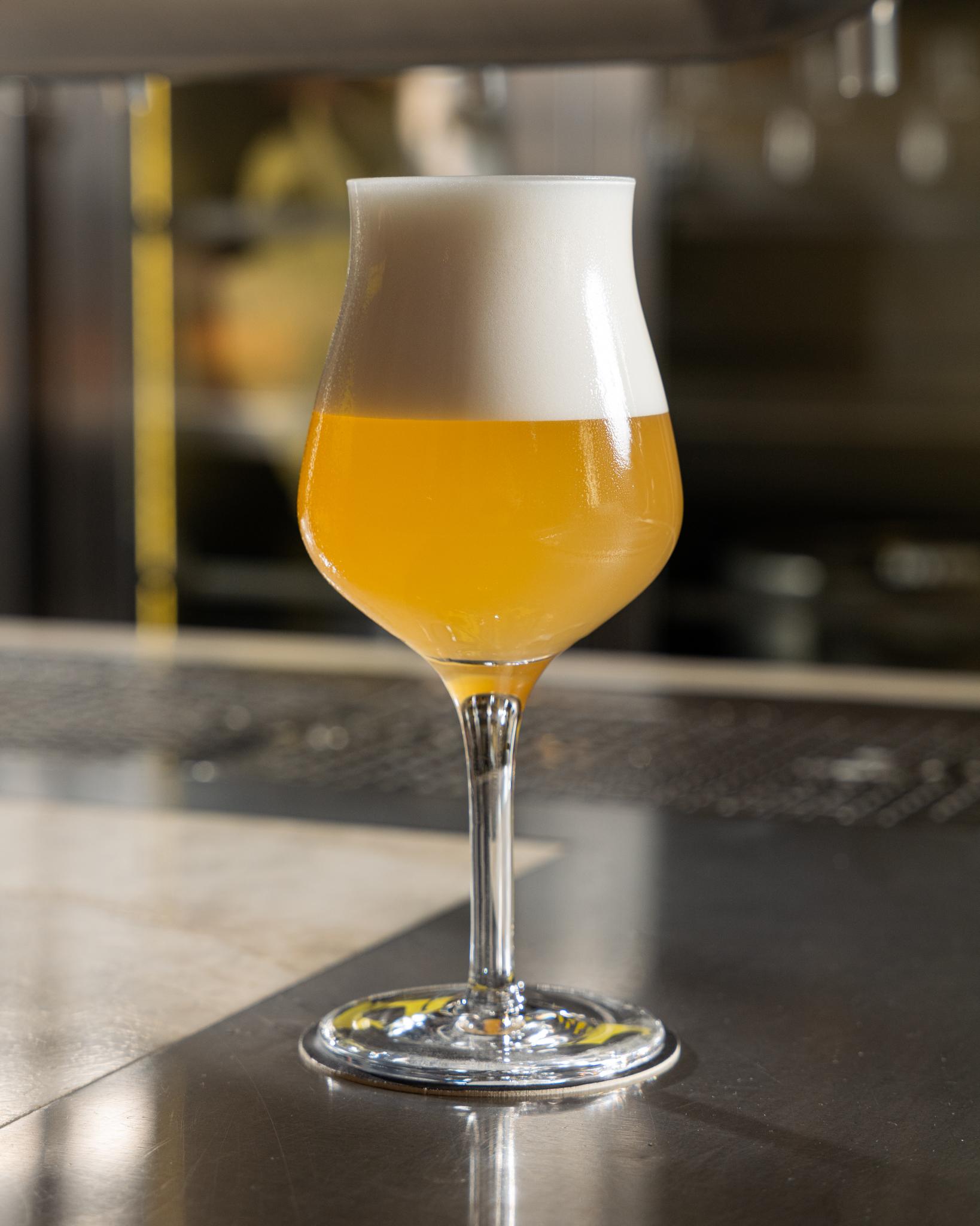 Sklenice craftového piva s hustou pěnou na barovém pultu.