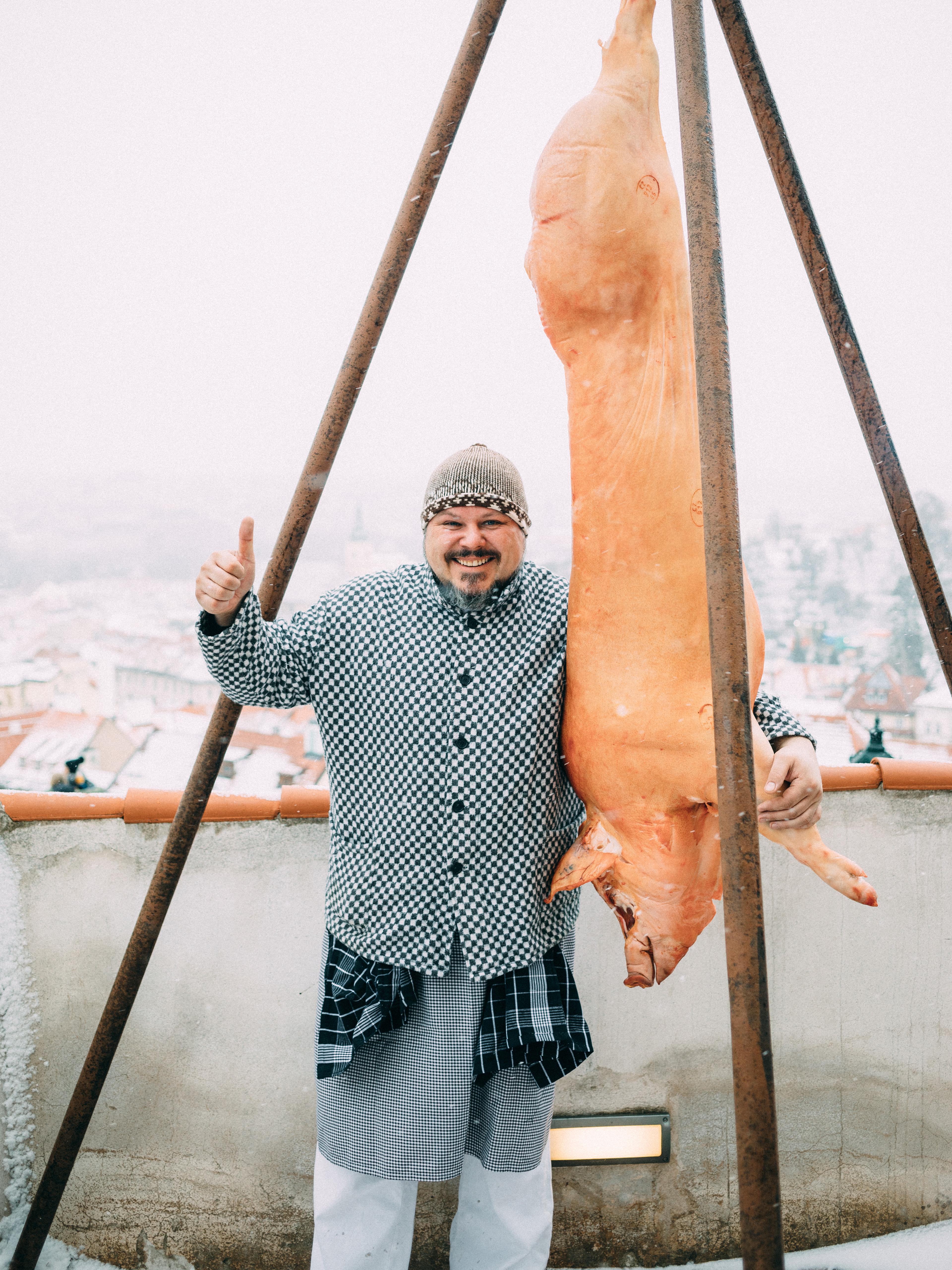 Kuchař při tradiční zabijačce s vyvěšeným vepřovým masem.