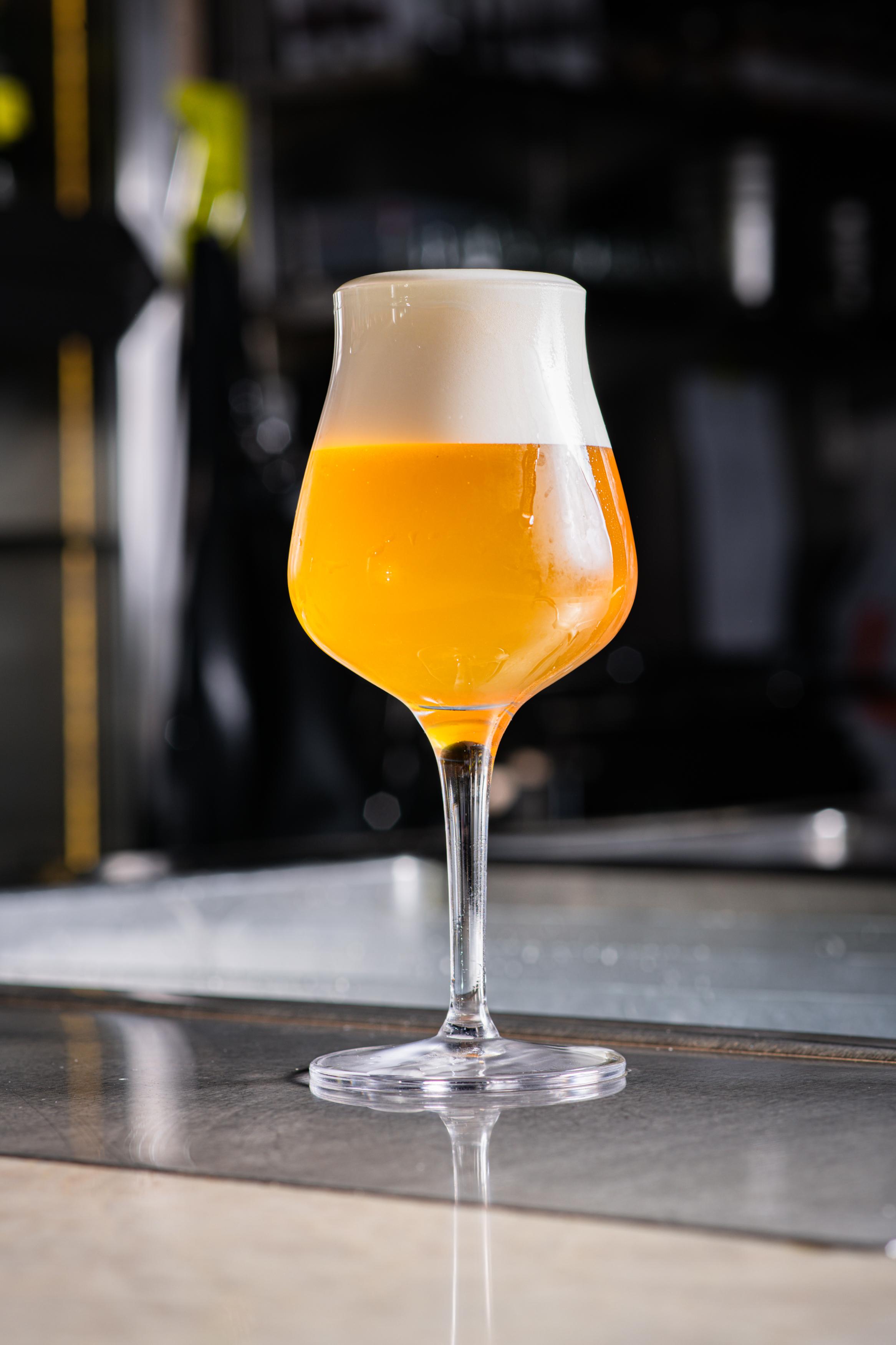 Sklenice světlého craftového piva s hustou pěnou na barovém pultu.