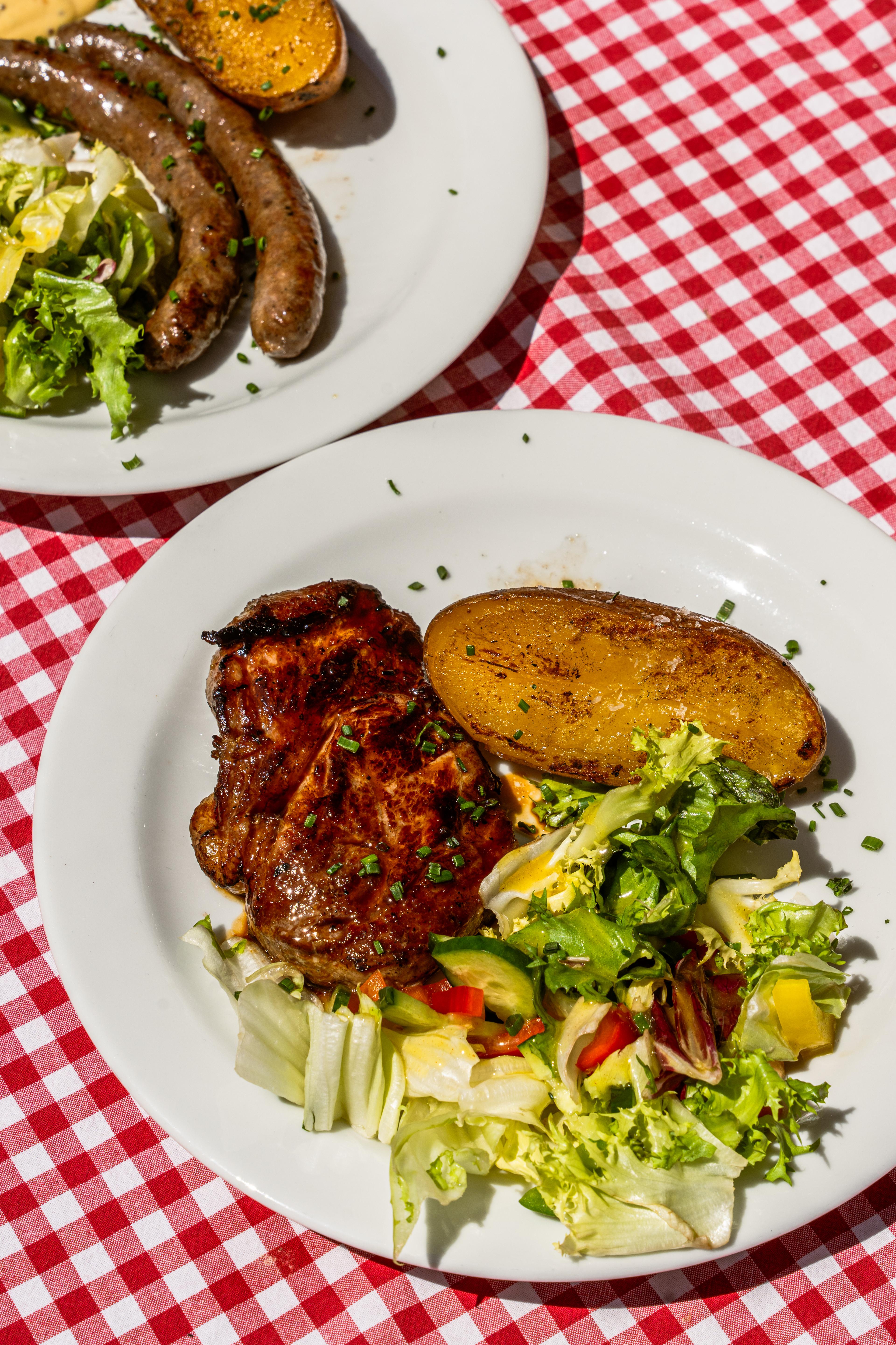 Grilovaný steak s pečenou bramborou a míchaným salátem na bílém talíři.