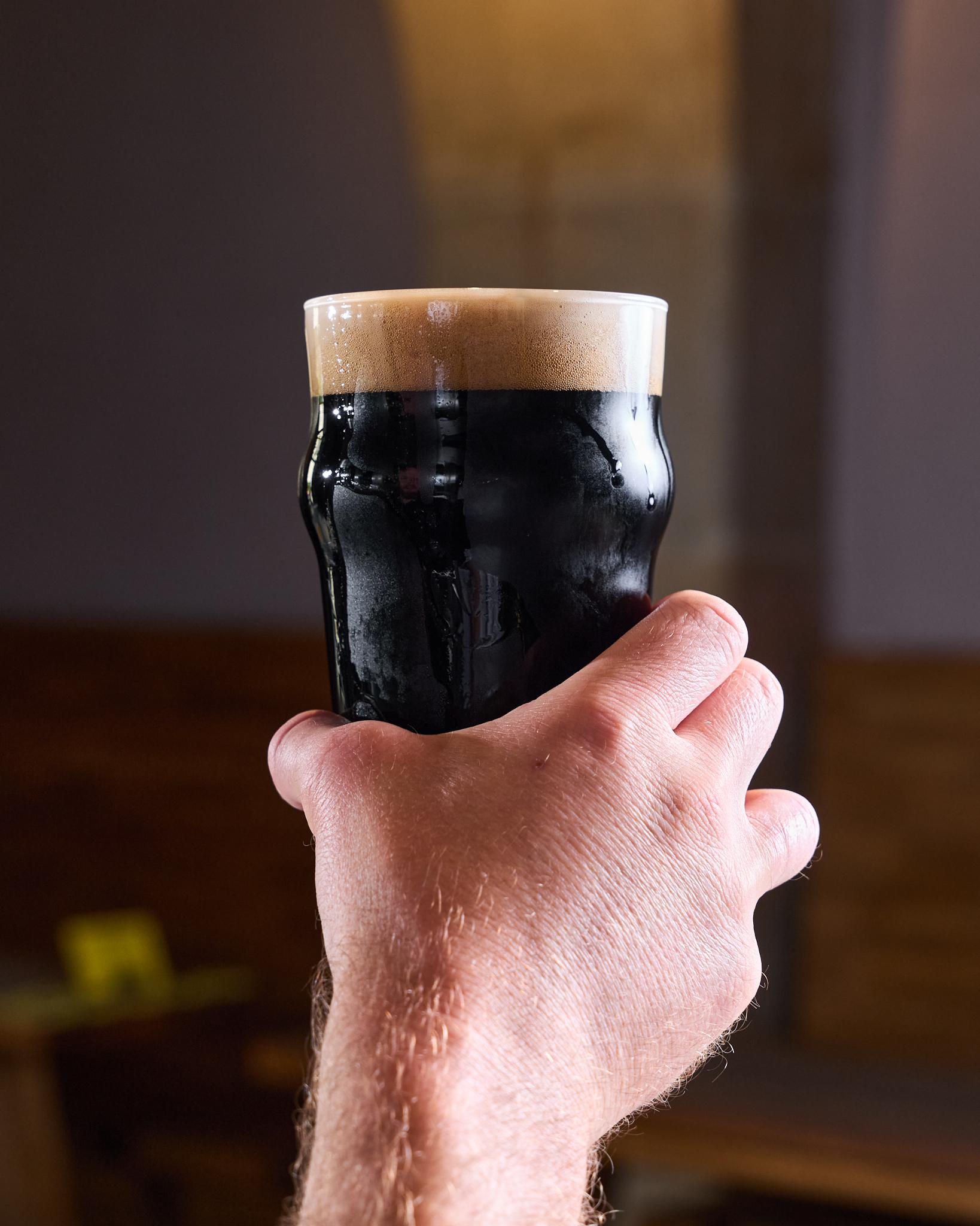 Sklenice Guinness s krémovou pěnou držená v ruce.