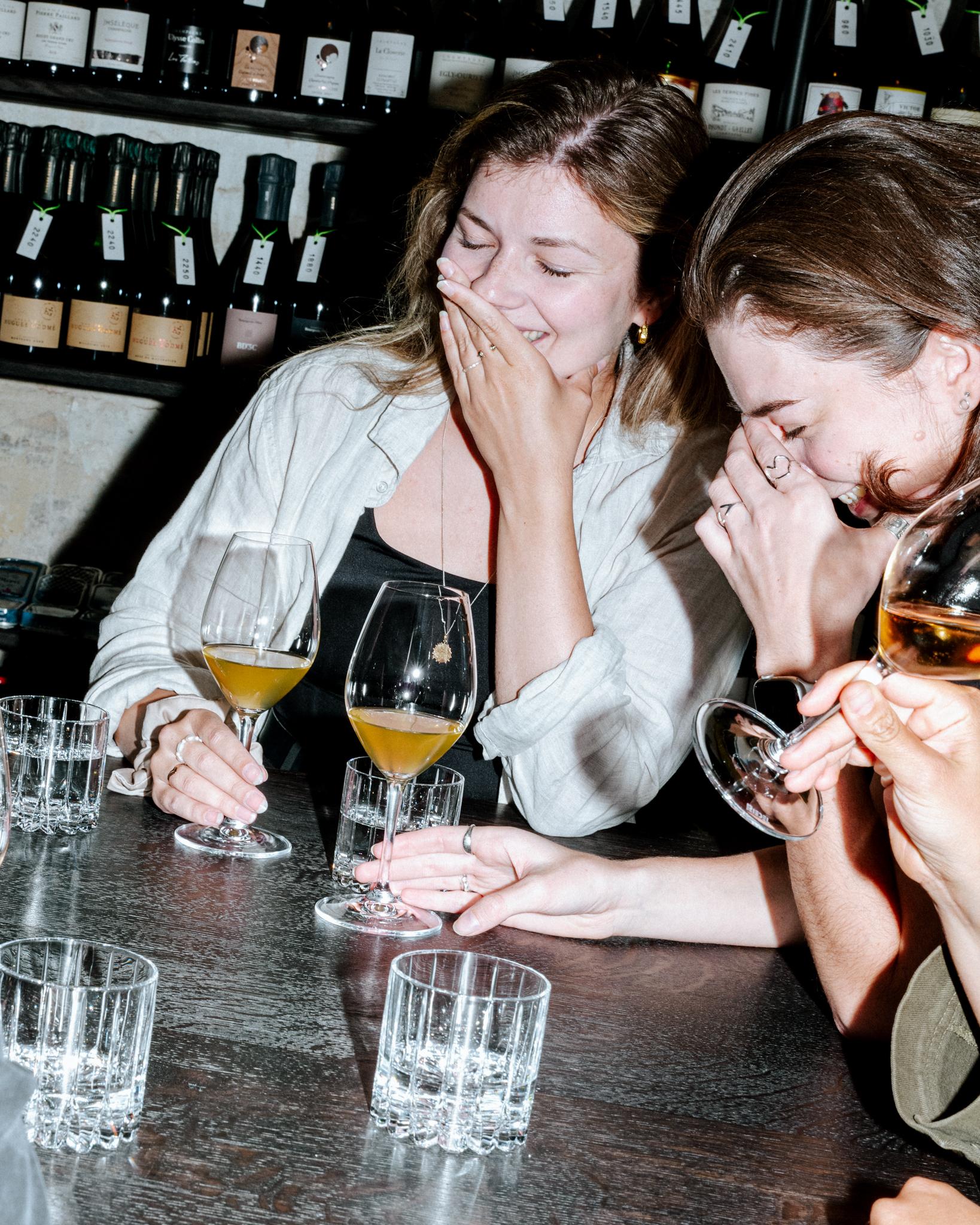Skupina hostů sedí u stolu s číšemi vína a během degustace se společně směje.