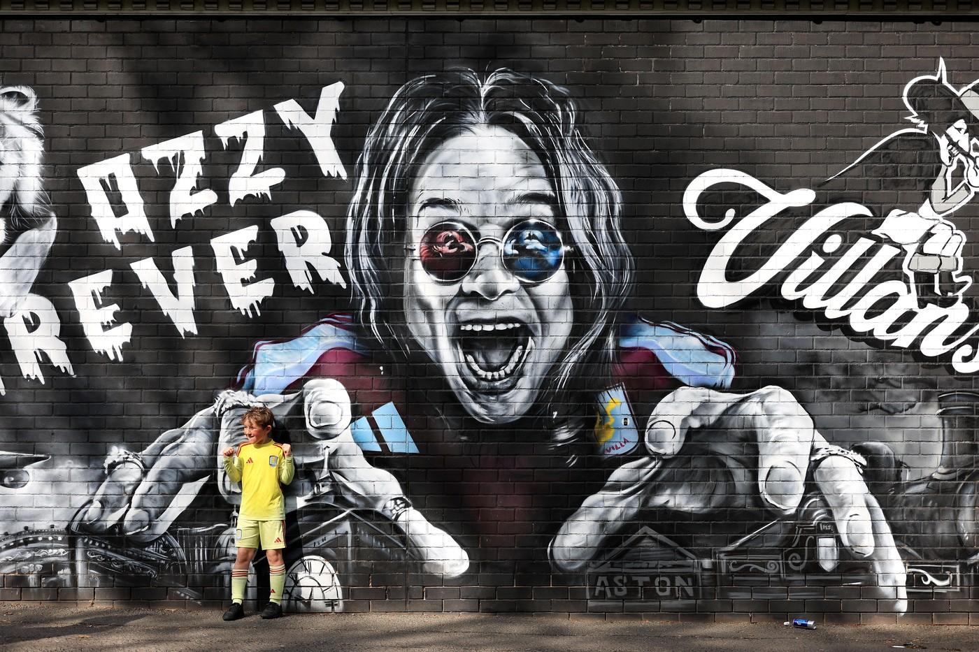 Fanoušek Aston Villy pózuje před nástěnnou malbou věnovanou Ozzymu Osbournovi v blízkosti stadionu před zápasem Premier League ve Villa Parku Fanoušek Aston Villy pózuje před nástěnnou malbou věnovanou Ozzymu Osbournovi v blízkosti stadionu před zápasem Premier League ve Villa Parku