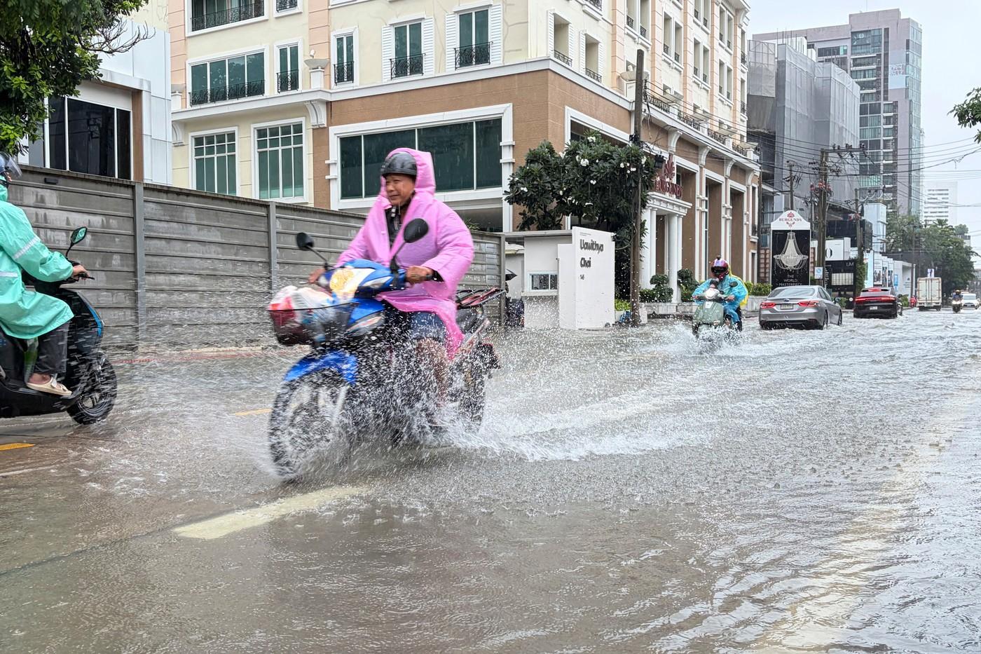 Na této fotografii pořízené smartphonem se lidé pohybují v záplavové vodě po silných deštích v Bangkoku