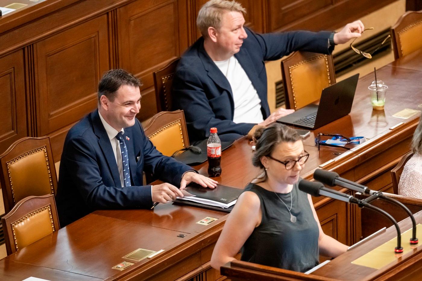 Ministr zahraničí Petr Macinka (Motoristé sobě) a ministr práce a sociálních věcí Aleš Juchelka (ANO) na schůzi Poslanecké sněmovny. U řečnického pultu hovoří poslankyně Pirátů Irena Ferčíková Konečná