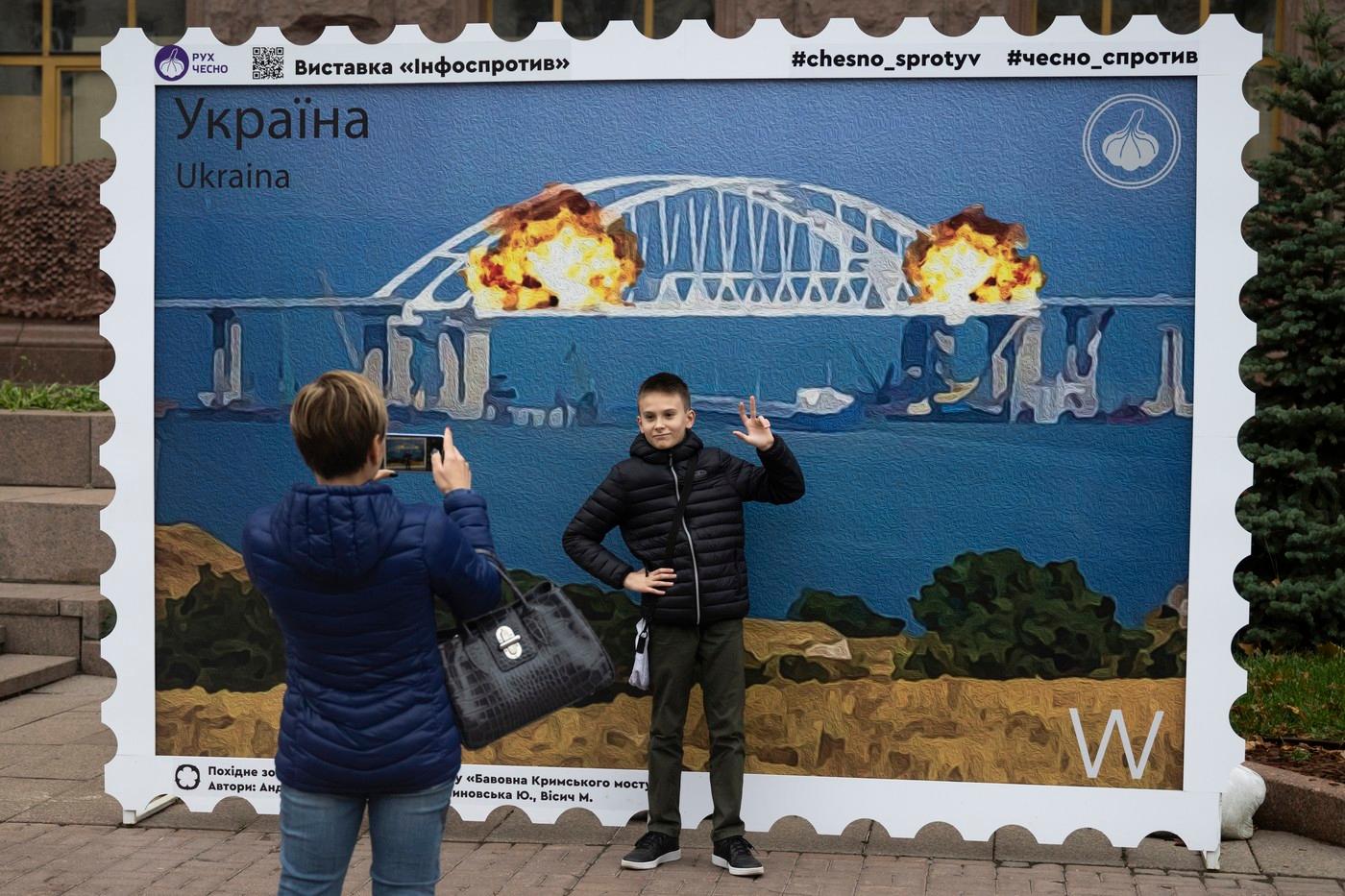 Ukrajinský chlapec pózuje u obrazu znázorňujícího první útok na Kerčský most, 4. listopadu 2022, Kyjev, Ukrajina.